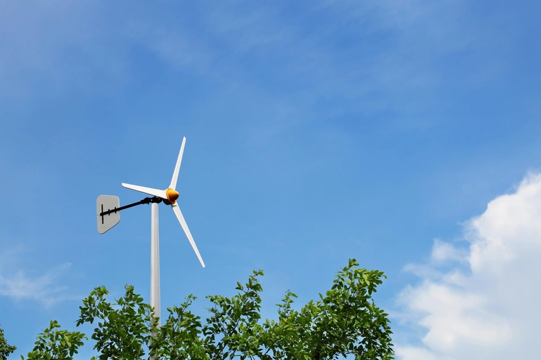 Malá domácí větrná elektrárna na modré obloze nad stromy.