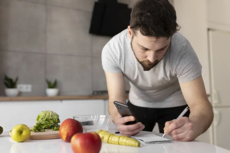 Muž počítá kalorie pomocí telefonu v kuchyni s ovocem.