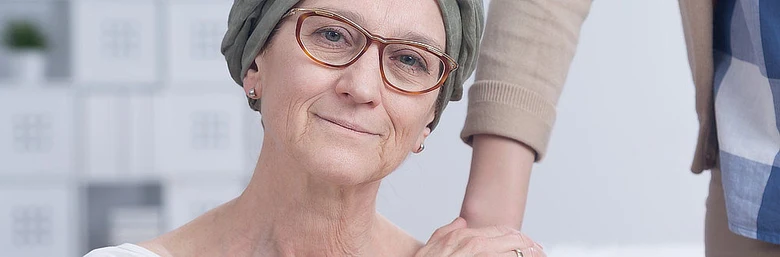 Žena s šátkem na hlavě se usmívá po léčbě rakoviny prsu.