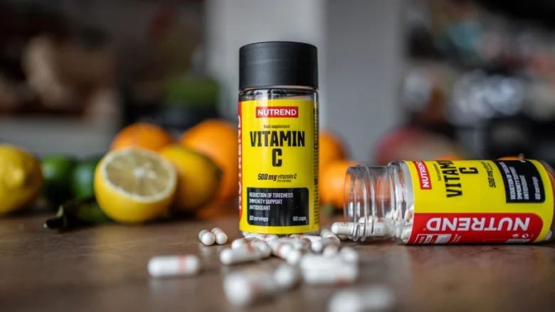Fľaše s vitamínem C a pilulky na dřevěném povrchu.