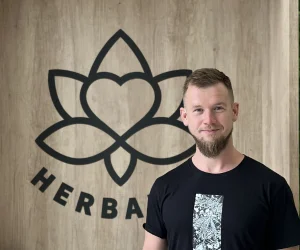 Muž stojí před dřevěnou stěnou s logem firmy.