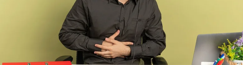 Muž sedící u stolu drží si ruce na břiše.