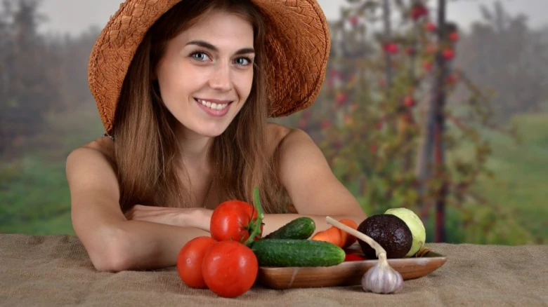 Žena s čerstvými zeleninovými produkty na venkovském stole.