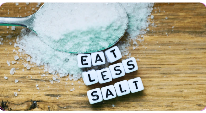 Lžíce soli s písmenky Eat Less Salt na dřevěném povrchu