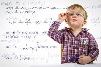 Malý chlapec s brýlemi u tabule plné matematických rovnic.