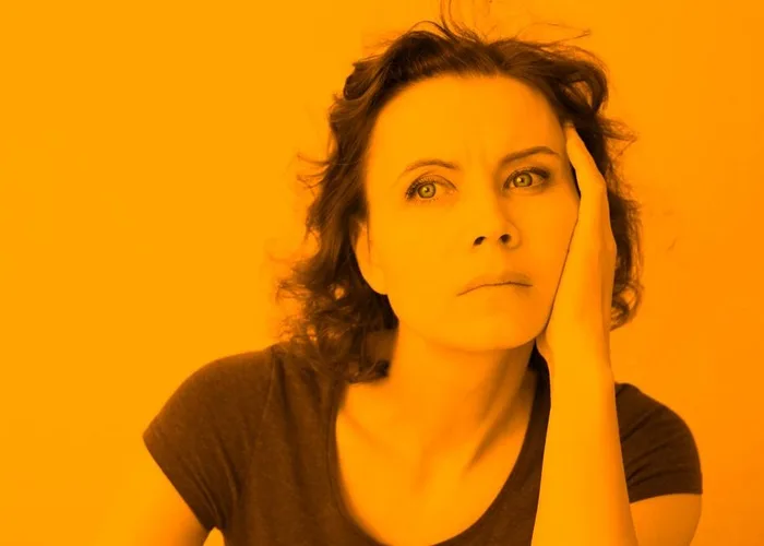Žena zamyšleně hledí nahoru s rukou u tváře.