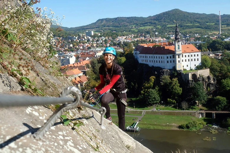 Žena v helmetu leze po ferratě nad městem s kostelem