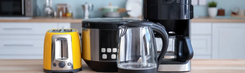 Žlutý toastovač vedle kávovaru a elektrického hrnce na kuchyňské desce.