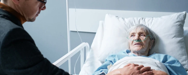 Starší žena s kyslíkovou maskou v nemocničním lůžku, která dostává paliativní péči.