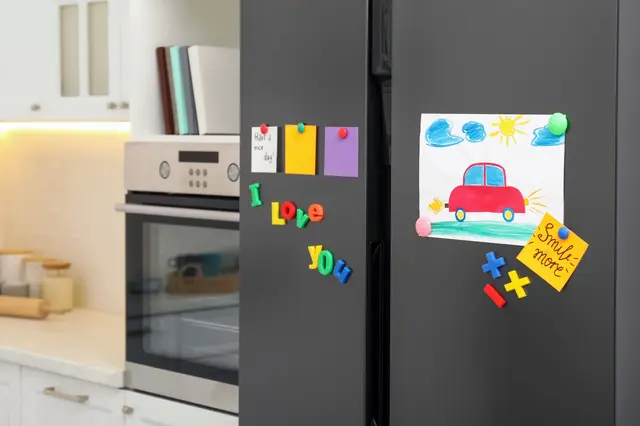 Černá lednice s dětskými kresbami a magnetickými písmeny.