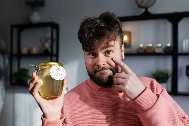Muž drží sklenici medu a ukazuje na tvář.