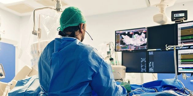 Chirurg v operační místnosti sleduje monitor s daty o srdečním rytmu.