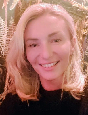 Usměvavá blond žena v černém tričku na pozadí.