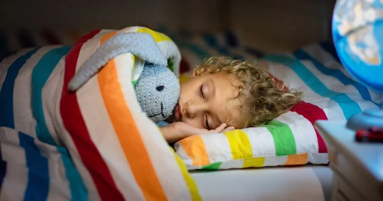 Spící dítě s hračkou v barevném dečkování.