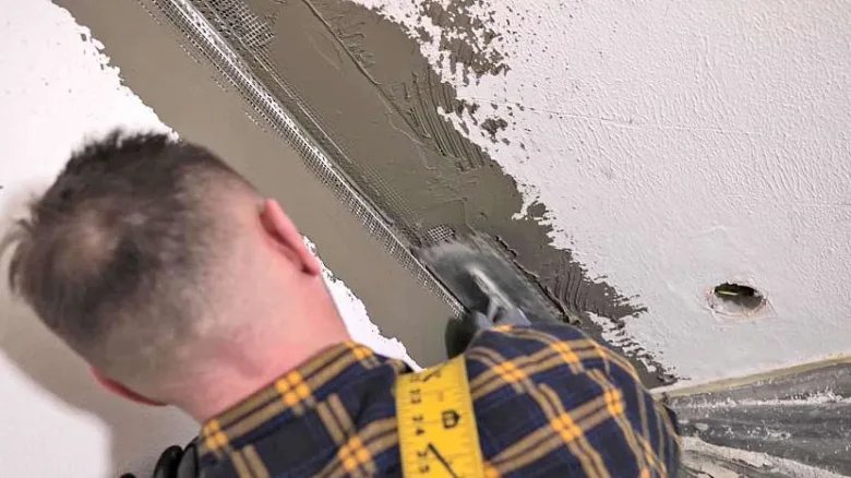 Muž natáčí perlinku na stěnu špachtlí s hmotou.