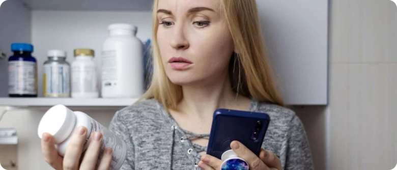 Žena kontroluje doplňky stravy pomocí telefonu v kuchyni.