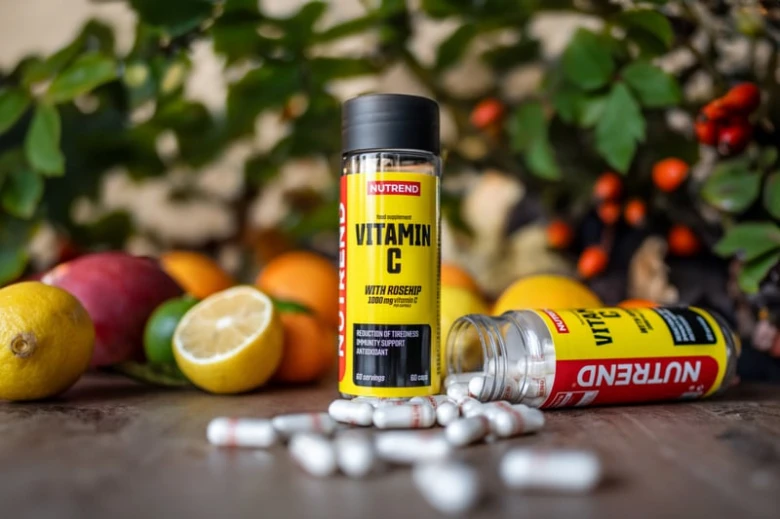 Skleněná lahvička s vitamínem C mezi čerstvými ovocnými plody.