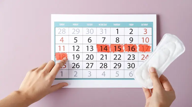 Kalendář s označenými daty a menstruační vložka na růžovém pozadí.