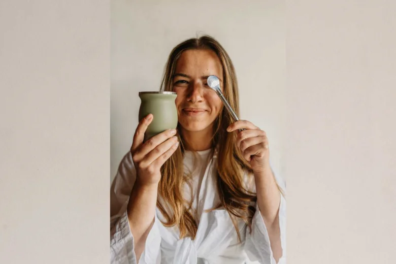 Žena drží šálek s nápojem a hračičně dotýká se oka lžící.