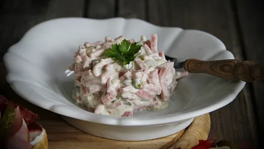 Pařížský salát v bílé misce s petrželkou na dřevěném podkladu.