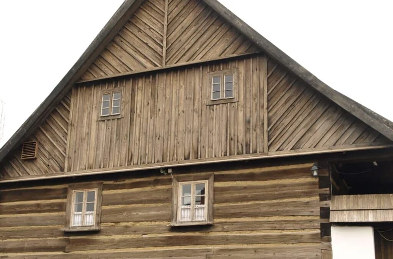 Tradiční dřevěný dům s roubenou konstrukcí na pozadí.