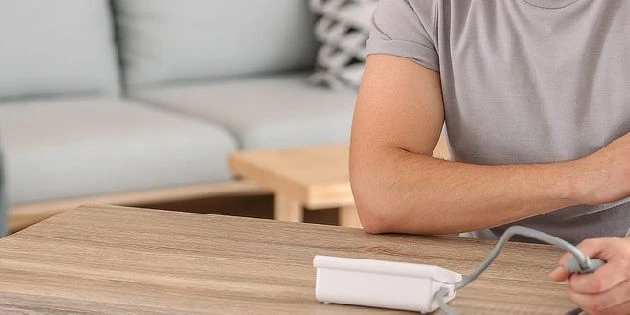 Muž měří svůj krevní tlak pomocí elektronického zařízení doma.