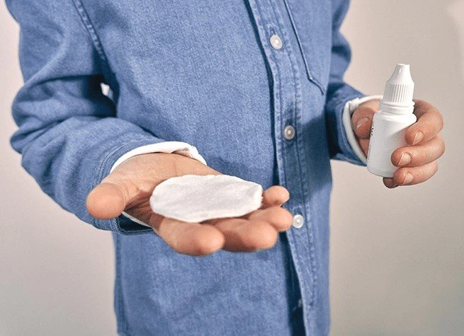Muž drží v ruce kapky do očí a vatový tampon.