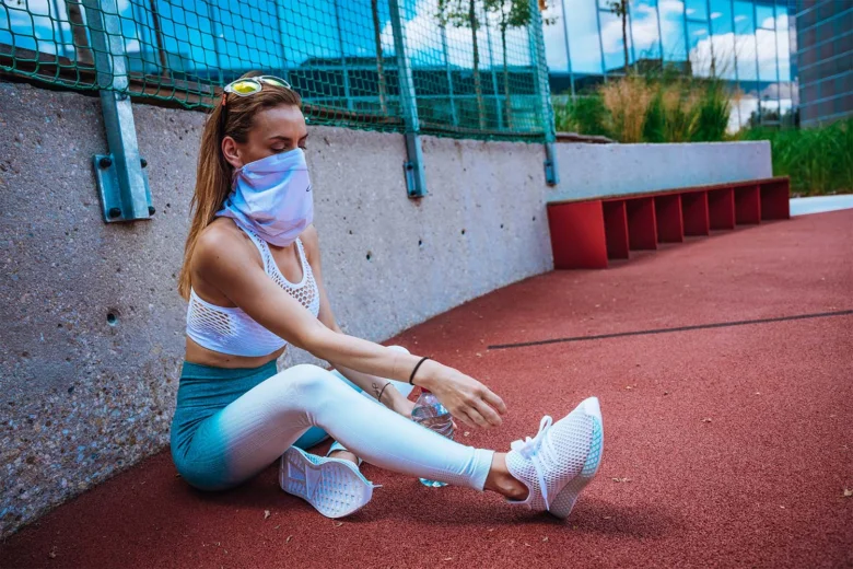 Žena v sportovním oblečení se natahuje na dráze s rouškou.
