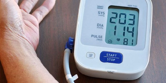 Digitální měřič krevního tlaku s vysokým čtením vedle ruky.