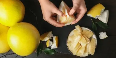 Ruční odstraňování slupky z celého žlutého pomeranče na tmavém povrchu.