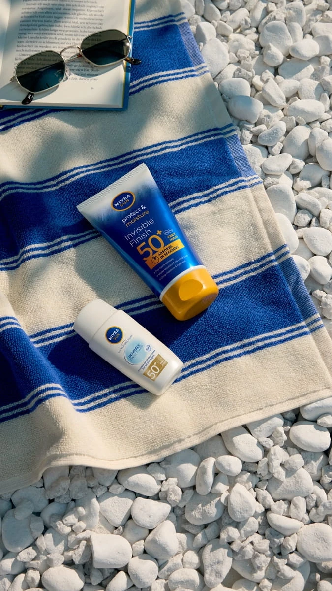 Dva krémy na opalování s vysokým SPF leží na plážovém ručníku.