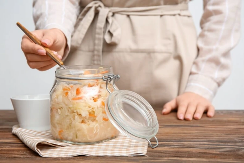 Fermentovaná zelenina v skleněné nádobě na kuchyňském stole.
