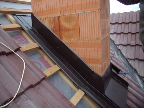Instalace černého oplechování na cihlový komín při stavbě střechy.