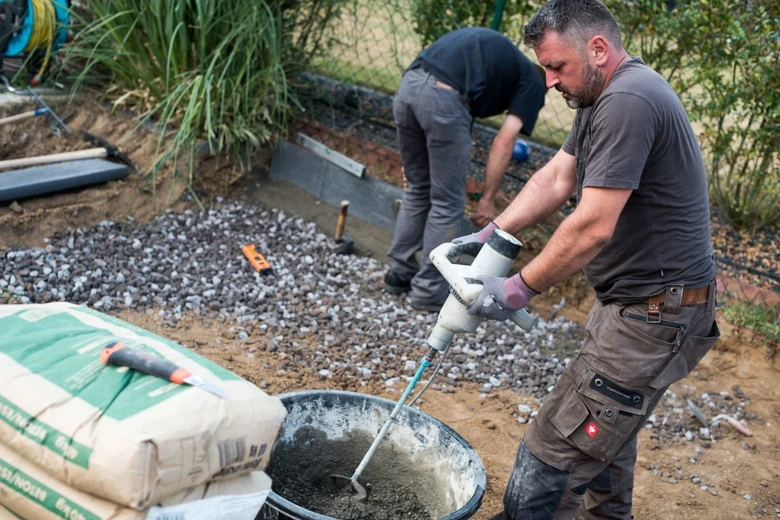 Muž míchá beton v kbelíku pomocí elektrického smíchávače.