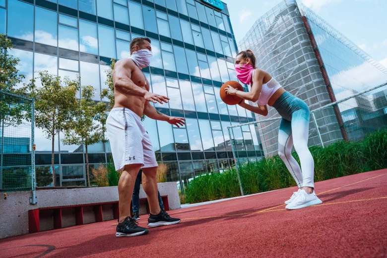 Muž a žena hrají basketbal venku před skleněnou budovou.