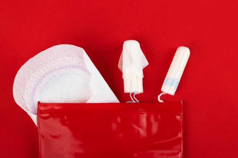 Červená taška s menstruačními vložkami a tampóny na červeném pozadí.