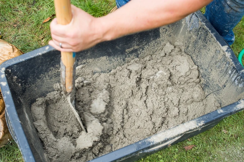 Míchání betonu rukou v plastovém kontejneru na trávníku.