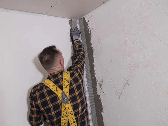 Muž natáčí perlinku na roh zeď pomocí špachtle.