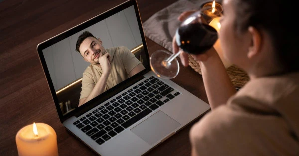 Žena pije víno u počítače s videotelefonem.