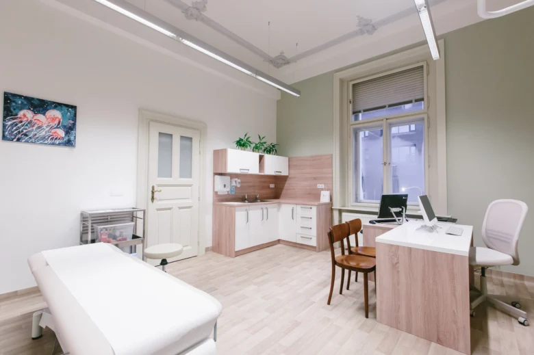 Moderní lékařský ordinace s vyšetřovacím stolem a kuchyňkou.