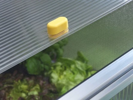 Žlutý ventilátor na střeše skleníku s rostlinami uvnitř.