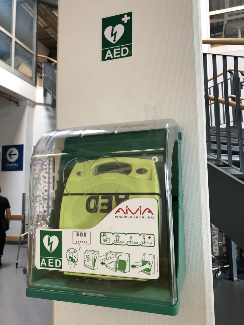 Zelený automatický externí defibrilátor v ochranném pouzdře na zdi.