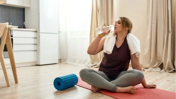 Žena pije vodu po cvičení s válcem pro relaxaci.