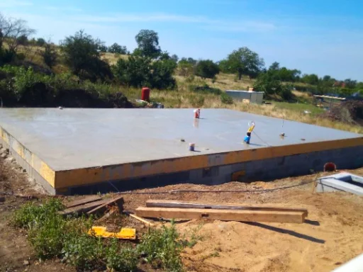 Čerstvě nalitá betonová podlaha na stavbě s dělníky.