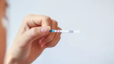 Ruka drží těhotenský test s dvěma čarami ukazující pozitivní výsledek.