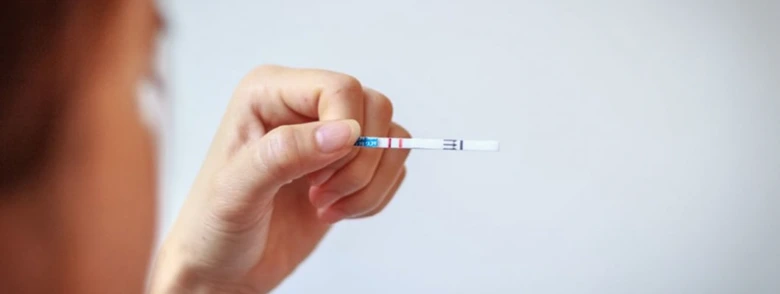 Ruka drží těhotenský test s dvěma čarami ukazující pozitivní výsledek.