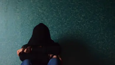 Osoba v kapuci sedí se složenýma rukama před obličejem.