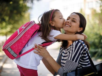 Girl kissing mother with backpack