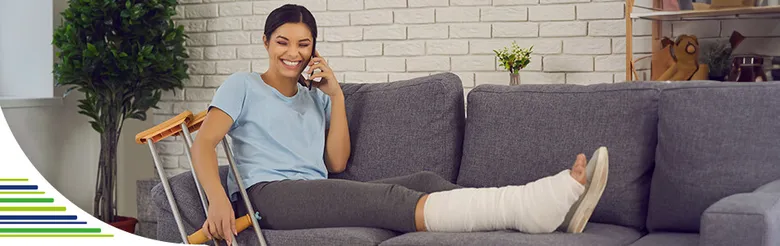 Žena s natrhaným nohou sedí na gauči a mluví do telefonu.