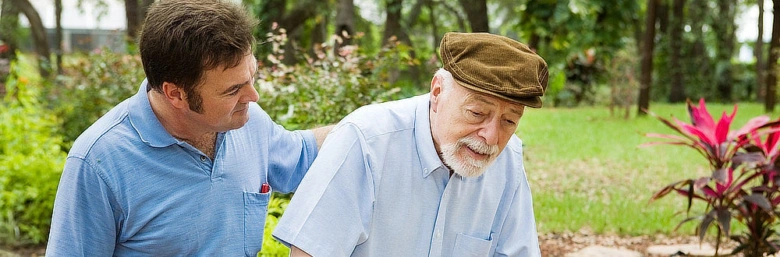 Muž pomáhá staršímu muži chodit venku v přírodě.